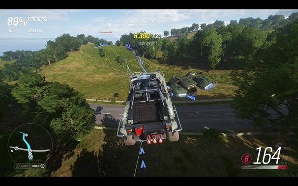 This is a screenshot from an off-road racing video game featuring a green all-terrain vehicle (ATV) with large tires and red accents on its sides, driving over rough terrain. The scene takes place during daylight with bright, natural lighting. The ATV is equipped with a black roof rack and has a red number 64 displayed prominently on the front. In the background, there are trees and the skyline, indicating an outdoor setting that could be a forest or jungle. There is no visible text overlaying the image. The color palette is dominated by greens, browns, and earth tones, contributing to an adventurous and rugged atmosphere typical of off-road racing games.