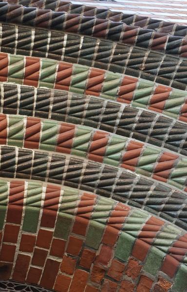 Très gros plan sur des rangées de moulures en briques avec une alternance de couleurs : une moulure en briques sombres, une moulure en briques rouges et vertes. L’extrémité des briques est bombé et lui-même mouluré pour que, une fois posées l’une à côté de l’autre, elles dessinent un motif torsadé. Le résultat est très coloré et rappelle les motifs des sucres d’orge.