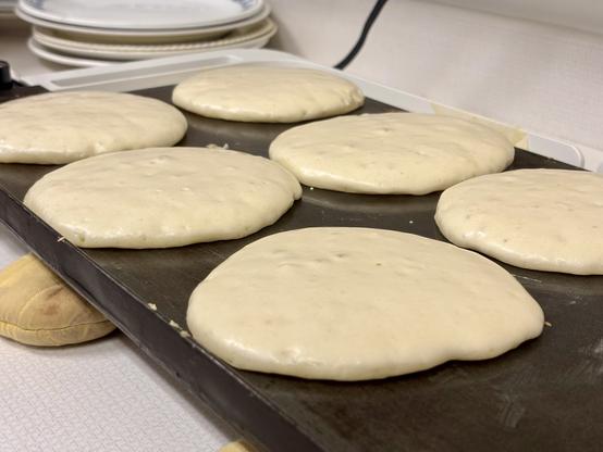 Six fluffy pancakes cooking on a griddle and looking delicious.