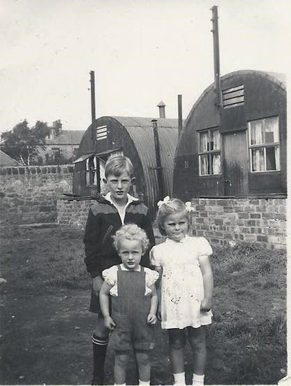 Elizabeth Kennedy with her big brother John and little brother Jimmy, standing outside the family's Nissen Hut at Lochinvar camp. Photo credit Elizabeth McArdle via Edinburgh Collected.