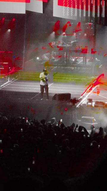 Chino Moreno, lead singer of Deftones, on stage, mic in hand. The image looks black and white, with streaks of red and green from the stage lighting surrounding him.