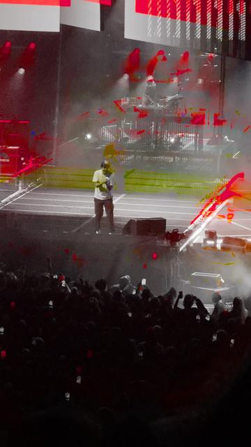 Chino Moreno, lead singer of Deftones, on stage, mic in hand. The image looks black and white, with streaks of red and green from the stage lighting surrounding him.