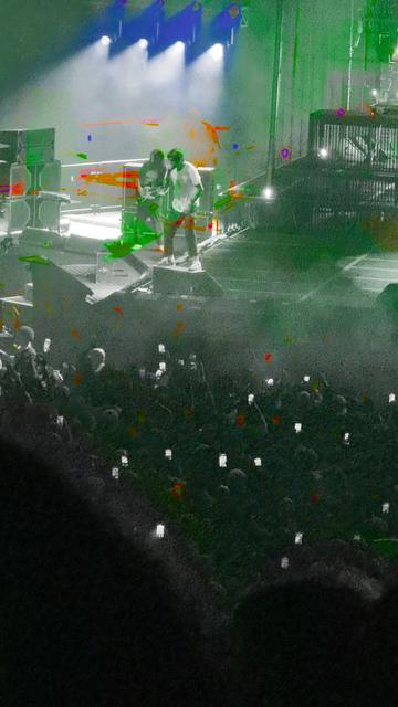Chino Moreno is singing next to the guitar player of Deftones. The image is saturated in various spots with blue, red, and green.