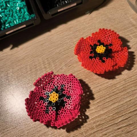 Two poppy flowers made out of Hama beads. One flower is a true red, the other one is made out of the bead color claret. Each flower has 4 petals and a black and yellow middle.