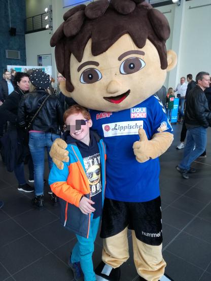 Ein Foto aus 2018. Ein neunjähriger Junge wird vor dem Heimspiel des TBV Lemgo von dem Maskottchen des Vereins in den Arm genommen.