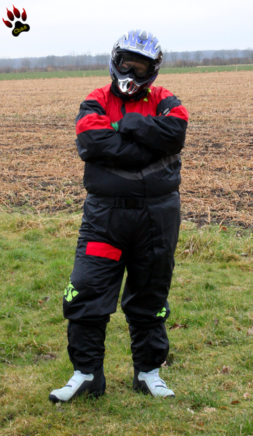 person wearing motocross raingear with boots and helmet, standing outside, looking into the camera with his arms crossed