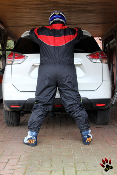 person wearing mx raingear, arms put up leaning to the back of a car, pictured from behind