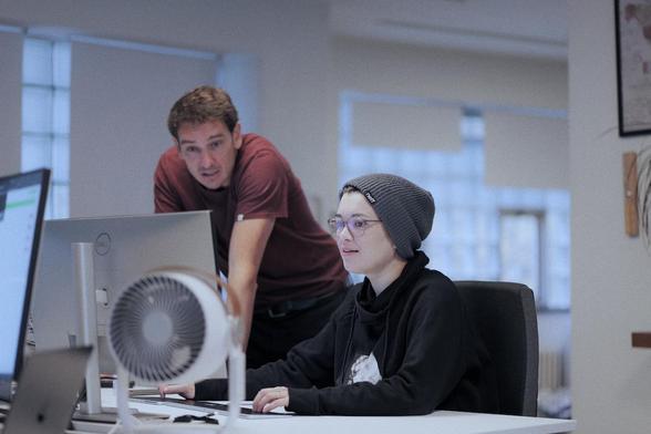 Zwei Personen, die an einem Computerarbeitsplatz etwas besprechen.