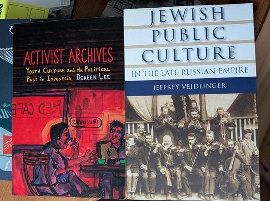 Two books placed side by side showing the covers. Activist Archives by Lee with a red-tinged painting of students discussing something in a cafe. Jewish Public Culture in the Late Russian Empire by Veidlinger which has a black and white photo of a 12-man Jewish orchestra on it.