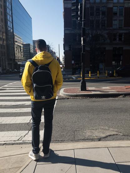 Man in a yellow jacket with a black backpack standing on a street corner