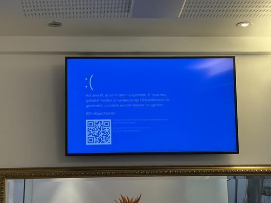 Ein Fernseher an einer weißen wand zeigt einen Windows Blue Screen. Direkt dadrüber die Decke, darunter ist noch der Rand vom Spiegel mit goldener Verzierung erkennbar.