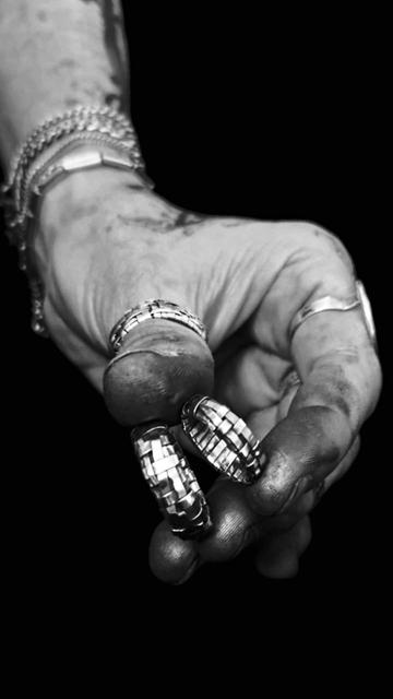 Black and white picture of a hand holding two woven rings handmade in silver ribbons, the working hand is dirty from the polishing.