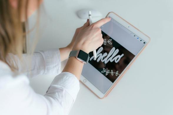 Une femme tient une tablette dans sa main gauche et affiche une montre connectée à son poignet droit.