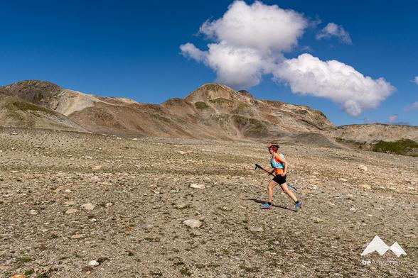 Woman trailrunning in the Swiss Alps on stoney terrain. Sunny day, blue sky, two white clouds above the mountains.
