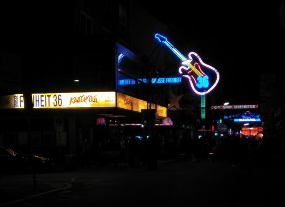 Nachtfoto. Großstadtstraßenszene. Neonröhren-Gitarre leuchtet. Große Freiheit 36 in Hamburg. Leute stehen im Dunkeln davor.