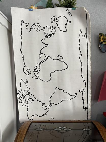 Black outline of a world map on canvas hanging sideways to dry. Missed GB and Ireland, so I’ll be adding them in once it’s dry!