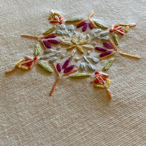 Flowers and leaves embroidered in a small mandala like pattern on a piece of white cotton