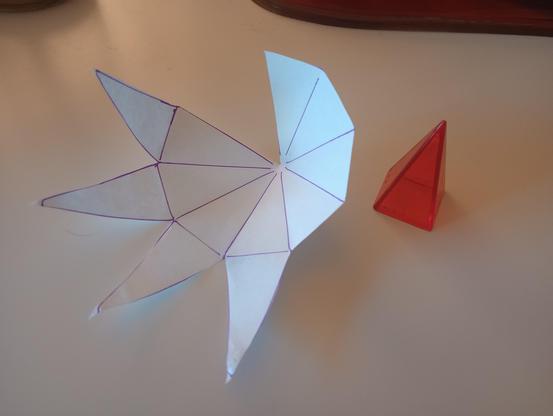 a hand-drawn, hand-cut template for a papercraft pyramid, next to a solid plastic pyramid of the same size