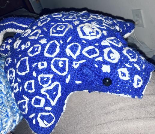 A bright blue and white stuffed spotted eagle ray plush. The main body is blue with white embroidered details to mimic the coloring of a spotted eagle ray. There is a black plastic safety eye on its face and there are attached gills near the eye like a spotted eagle ray would have in the wild.