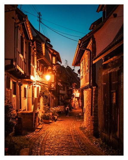 Dusk settles over a cobblestone street, where a lamp casts a warm glow, enhancing the tranquil scene.