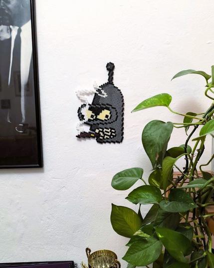 A "Bender" out of Hama beads. Bender is a character from the show Futurama. He's a robot and known for being rude, for smoking and drinking a lot. In this bead creation he's smoking a big cigar. The creation is the head, holding a cigar with smoke around his head.
