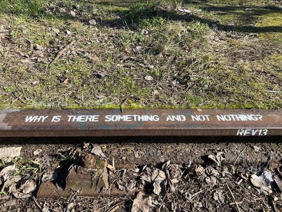 Photo of stencil graffiti on abandoned rail with white text ‘Why Is There Something And Not Nothing?’