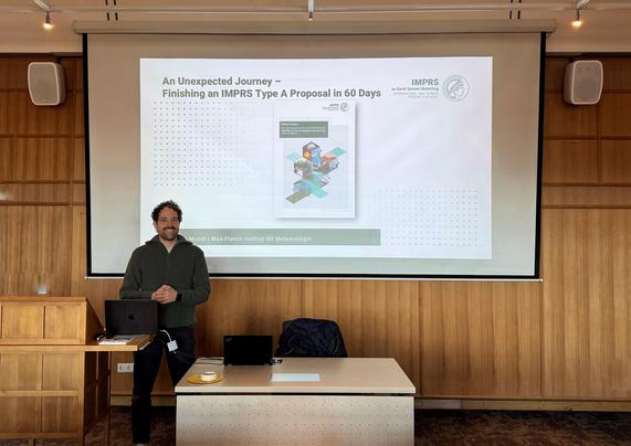 Florian Mundt in front of a slide projected unto a wall in a seminar room with wooden tiling.