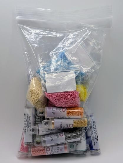 A plastic bag filled with tubes and baggies of delica and seed beads in various colors.