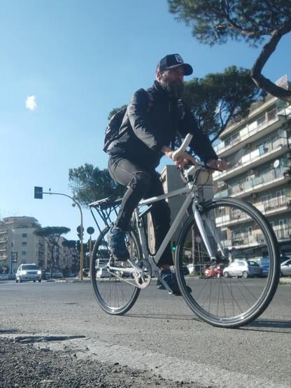 Un uomo con la barba va in bicicletta in ambiente urbano.