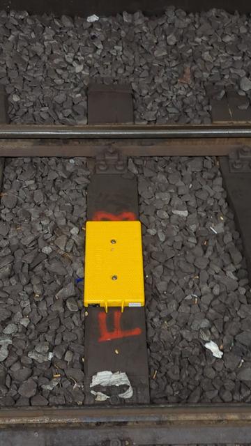 Nahaufnahme einer gelben Balise auf einer Bahnschwelle. Es ist der Siemens Schriftzug zu erkennen
