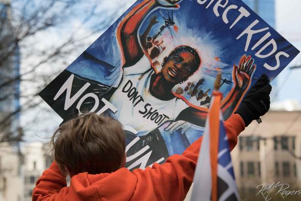 A child hold a protest sign aloft with the words “Don't Shoot Protect Kids.”