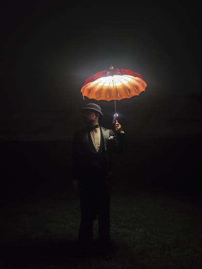 It's night. It's dark and all around me I'm enveloped in the inky black of nothing. Dressed in my best antique French tuxedo I hold aloft a glowing red and orange parasol. Civilization is far from me. There is a faint outline of mountains in the far inky distance behind me. No people, no city, nothing. Just me. Alone in the universe as a tiny spec of light. "Hello void."