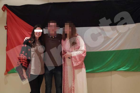 La poli infiltrada amb els ulls tapats per un rectangle blanc superposat, amb dues persones amb cara pixel·lada, davant d'una bandera palestina molt gran, posant per a la foto