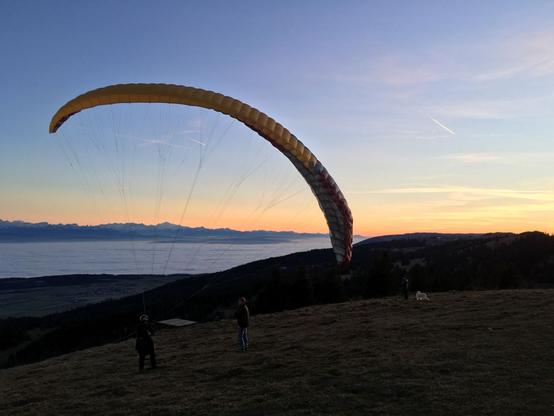 Un parapente sur le point de décoller avec une mer de nuage et un coucher de soleil en arrière plan.
