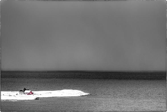 Schwarzweissfoto mit Selektivfarbe Rot für ein norwegisches Haus auf einer schneebedeckten Insel.