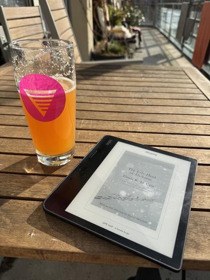 The same beer glass is now half empty sitting on a table outside in the sun next to an ebook reader.