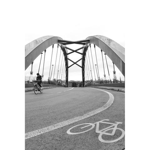 A cyclist on the left, a bike painted on the right, and two symmetrical arches of a bridge in the background.