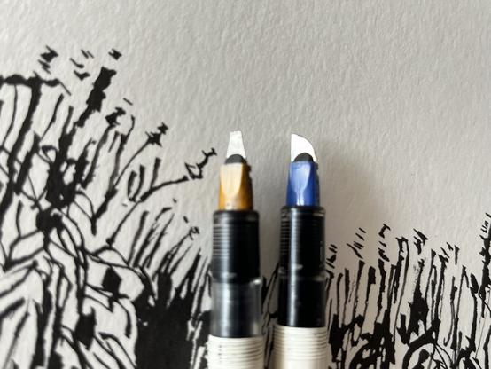 A close up of two Parallel Pen nibs: an unmodified 2.6mm at left, and a modified 6mm at right showing a parabolic edge.
