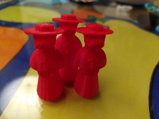 3 small otter figurines 3d printed with red filament. They are about 5cm tall, standing up and dressed like the Spanish Inquisition in long robes with flat hats and a cross necklace.