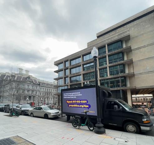 A black mobile billboard truck parked near the Consumer Financial Protection Bureau headquarters in D.C. On the side of the truck, a LED screen reads: Are (were) you a government worker? ProPublica journalists want to hear from you. Signal: 917-512-0201. propublica.org/tips.