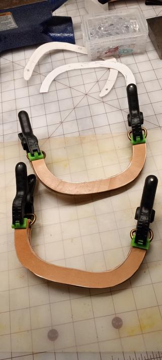 The same pieces of leather however the pieces without the hardware are glued onto each side of the pieces with the hardware. This makes two handles with a piece of filler leather on each side of each handle, three pieces of leather each. The ends are clamped into place with green and black spring clamps whilst the glue dries.