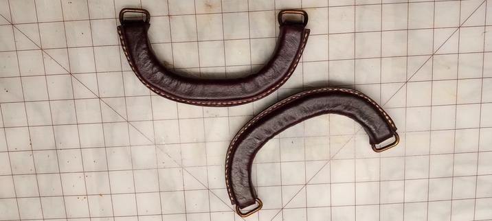 Two handles, one with ends facing up and one with ends facing down, that have had their wrapping stitched onto them and have been dyed mahogany brown.