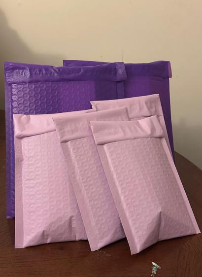 Two purple bubble mailers and four smaller light mauve pink bubble mailers propped up against each other on a wooden table