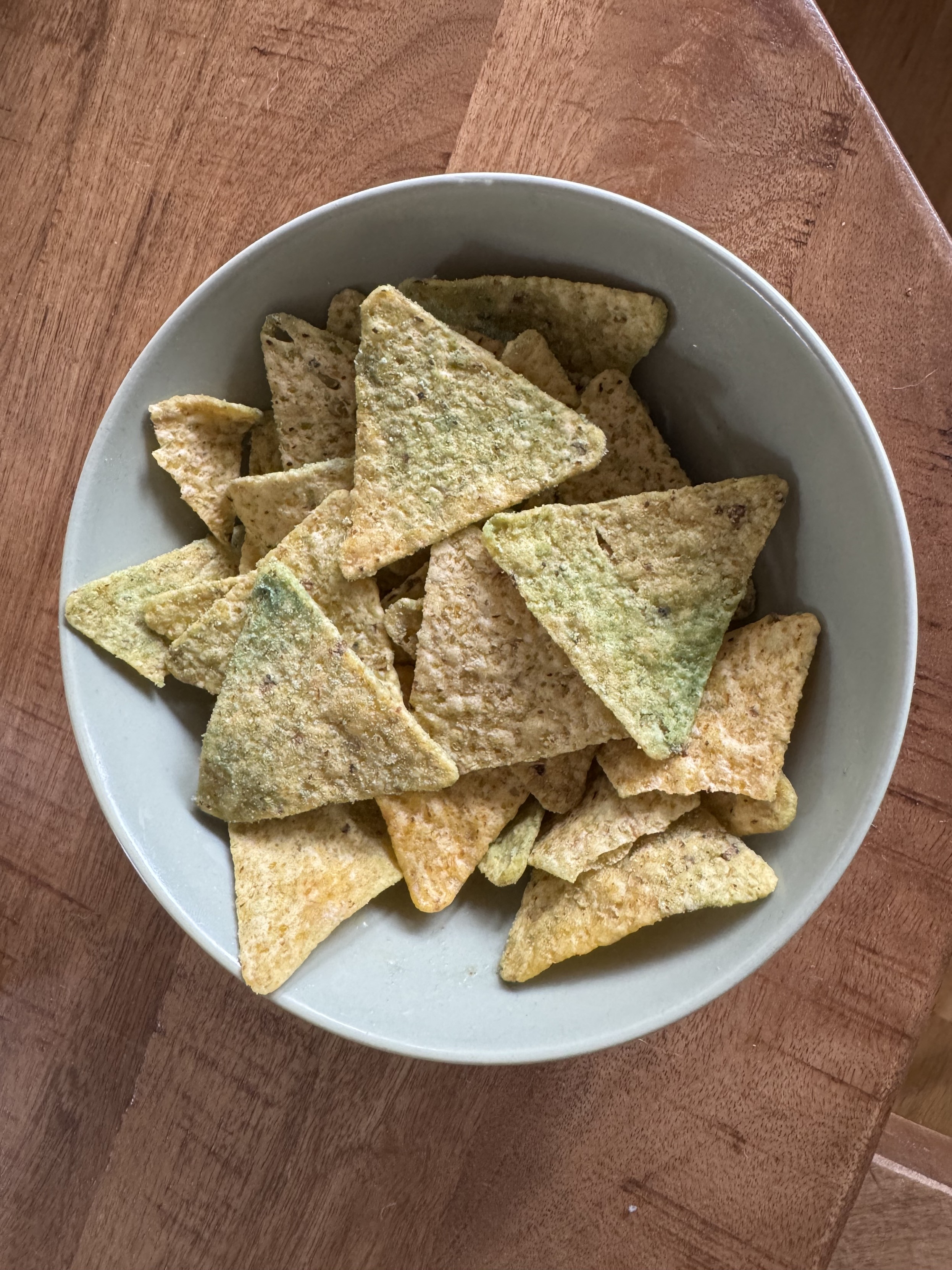 A photo of a bowl of nachos covered in green spices. Or mold.