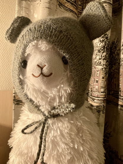 Alpaca stuff-toy wearing a baby bonnet with bear ears.