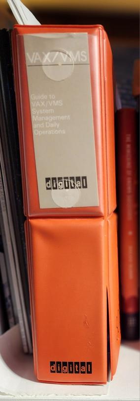an orange padded binder with a black D|I|G|I|T|A|L logo on the bottom of the spine. the binder contains a guide to daily VMS sysadmin tasks