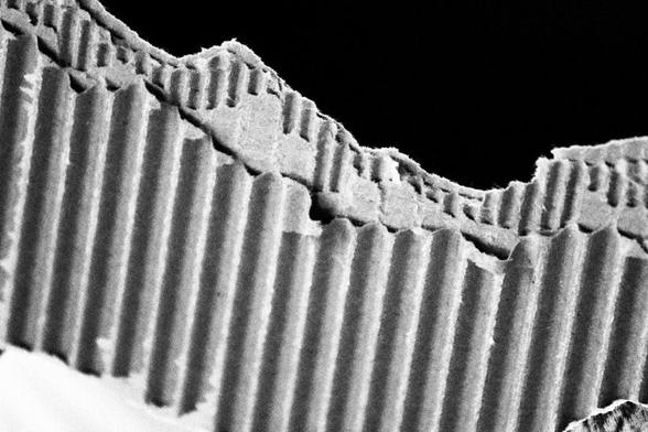A torn edge of corrugated cardboard creates an abstract impression of mountains against a pitch black sky.