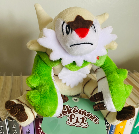 The Pokemon Fit plush Chesnaught is sitting on top of my books with a rather petulant expression. Chesnaught is a grass Pokemon, is one of the three Kalos starters, and I don't know exactly what it's supposed to be really but it's a big hulking mammalian creature with cream and green-colored appendages and a spiky shell on its back. Right now in its miniature plush form it's just hunched over and looking grumpy.