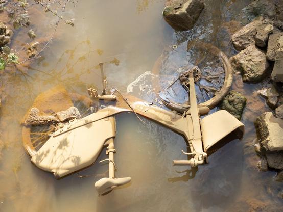 Bike caked in mud lying in a shallow muddy stream
