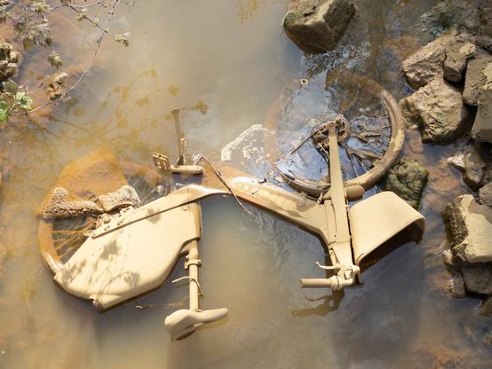 Bike caked in mud lying in a shallow muddy stream